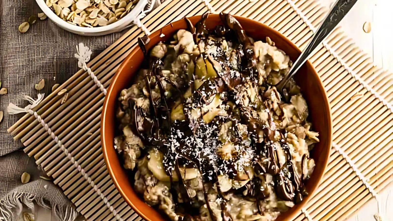 A bowl of oatmeal topped with chocolate drizzle, seeds, and coconut flakes, placed on a bamboo mat.