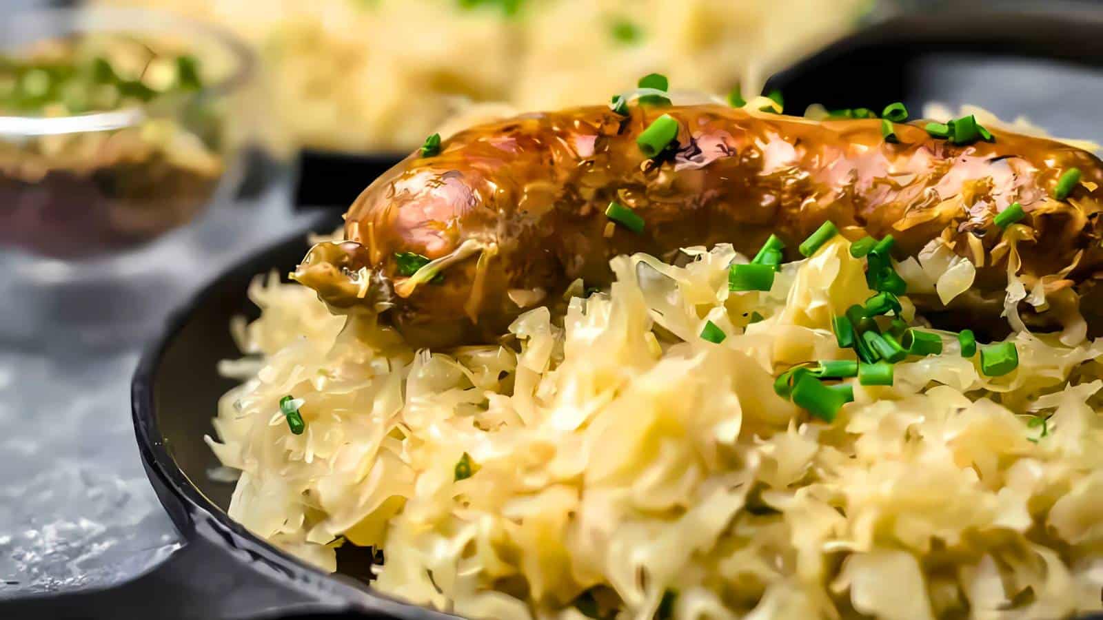 Sausage on a bed of sauerkraut, garnished with chopped chives, served in a black dish.