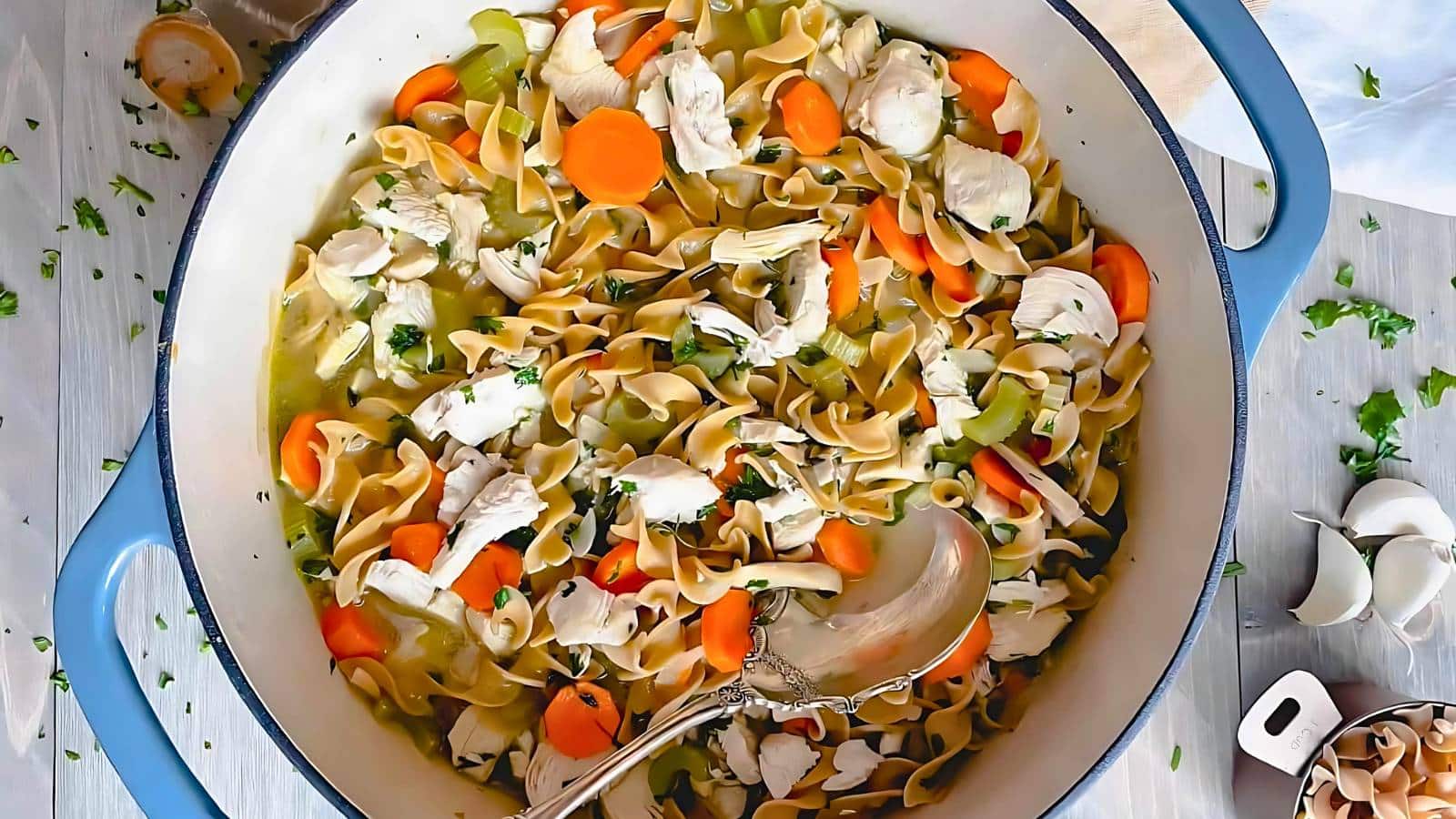 A pot filled with chicken noodle soup, featuring sliced carrots, celery, and parsley, with a ladle resting inside.