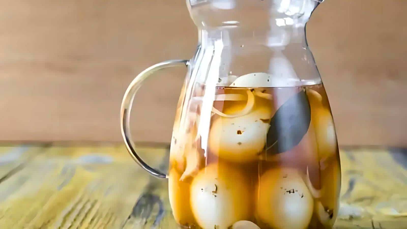 A clear jar filled with pickled eggs in brine sits on a wooden surface.