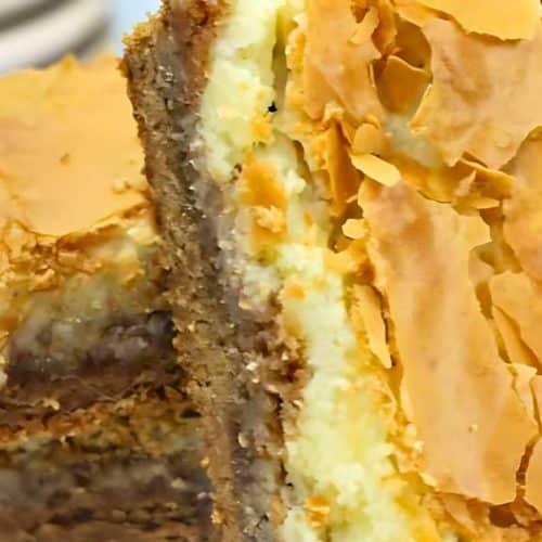 Close-up of layered dessert bars with a flaky top and creamy filling on a white plate.