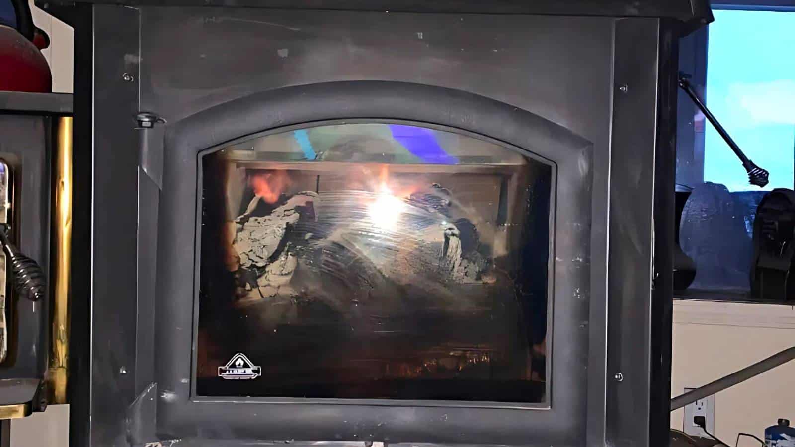 A glass-fronted wood stove with a fire burning inside. A window with a blue sky is visible to the right.