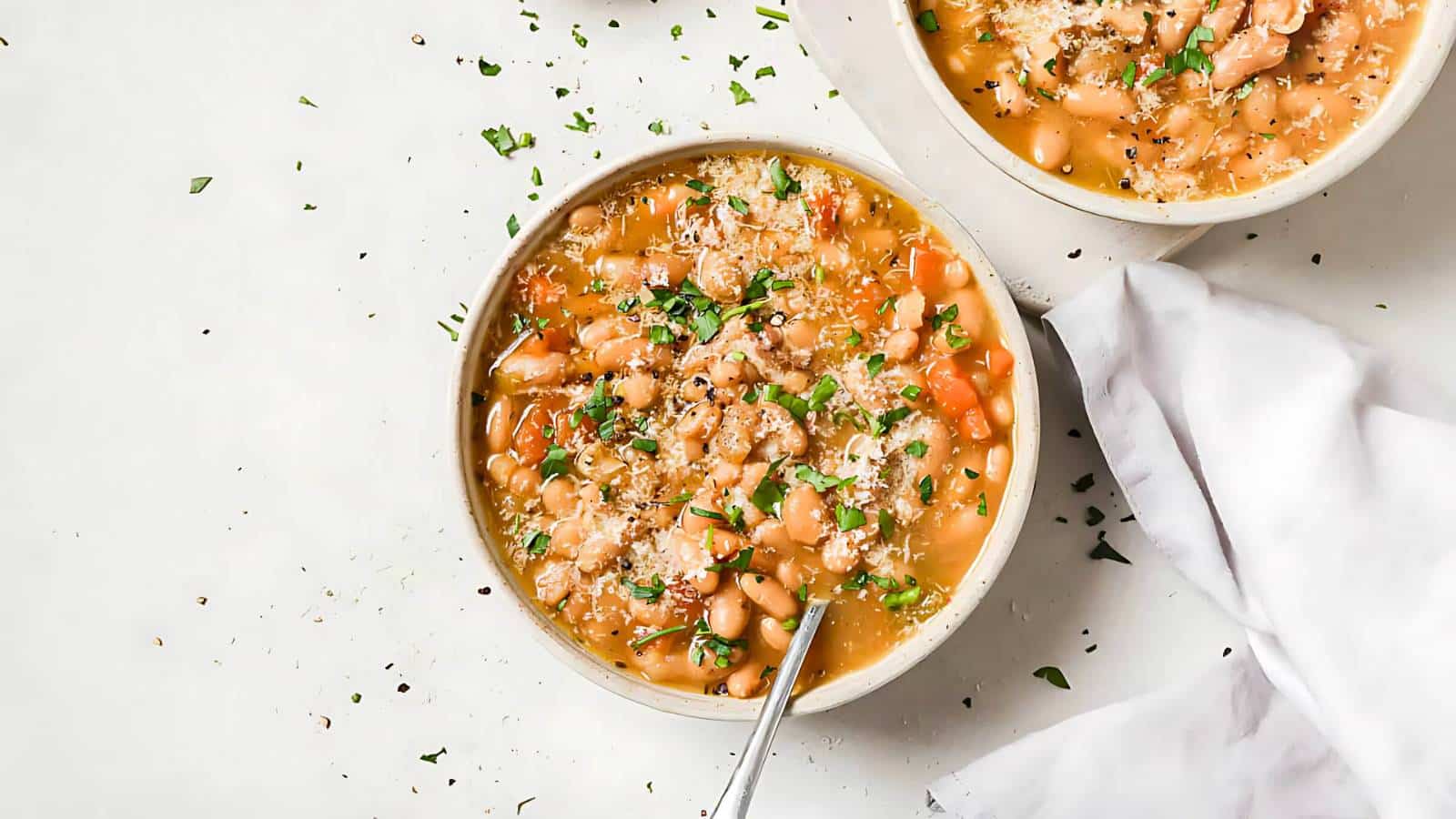 A bowl of bean soup topped with herbs and grated cheese, alongside a white napkin.