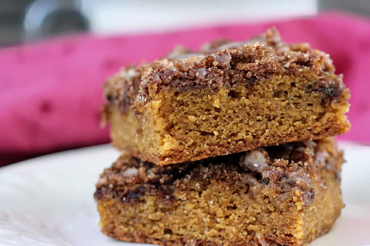 Two stacked slices of crumb-topped pumpkin coffee cake on a white plate, with a pink cloth in the background.