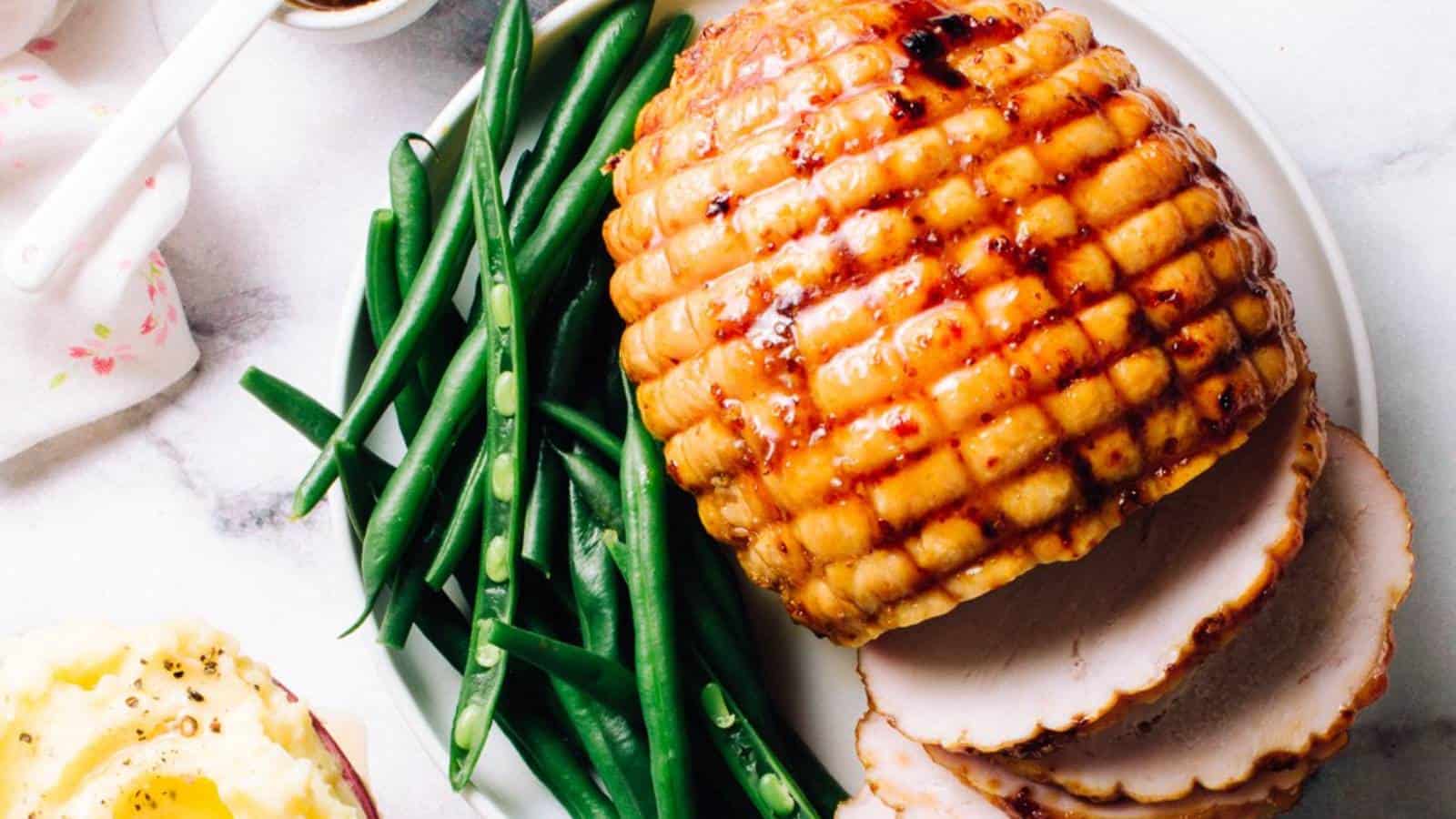 Roasted ham with a glazed crust served with green beans and sliced on a white plate.