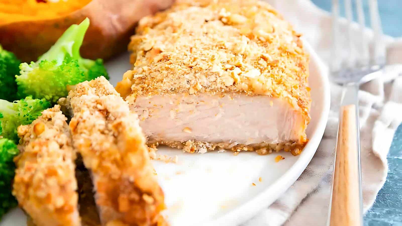 A plate with sliced, breaded chicken breast, broccoli, and a halved sweet potato. A fork is placed beside the plate.