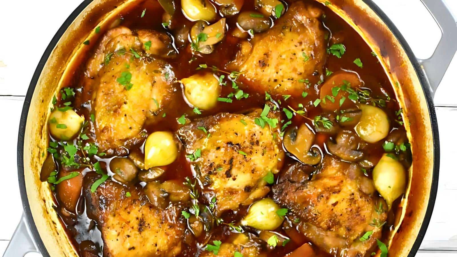 Cooked chicken thighs in a pan with mushrooms, onions, and a rich sauce, garnished with chopped parsley.