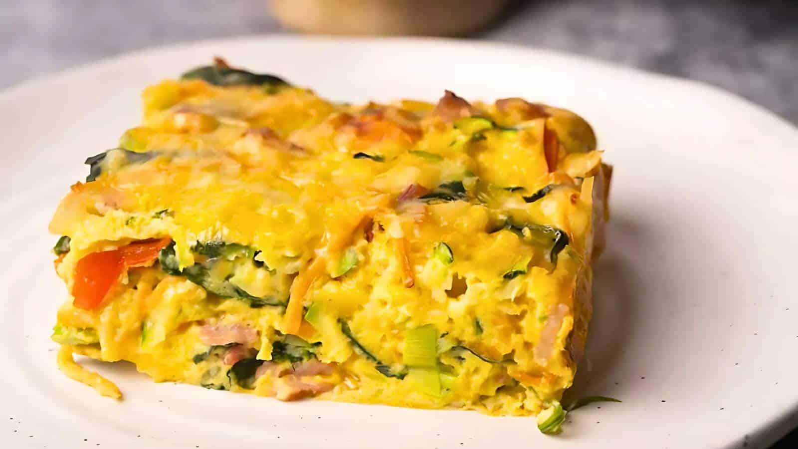 Slice of vegetable and cheese frittata on a white plate, featuring visible layers of spinach, tomatoes, and melted cheese.