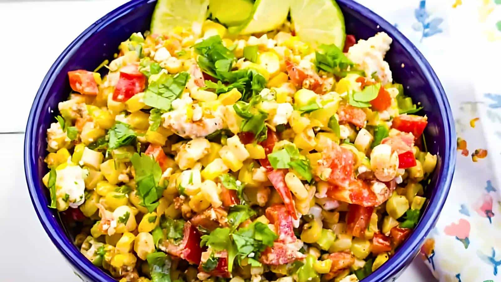 A bowl of diced avocado, cucumber, tomato, and cilantro salad on a striped cloth, with two spoons beside it.