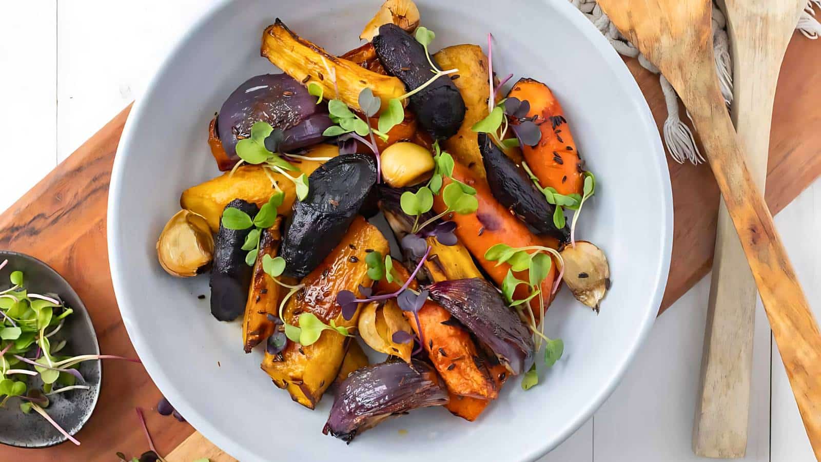 A bowl of orange lentil soup garnished with a bay leaf is placed on a white table with a silver spoon nearby.
