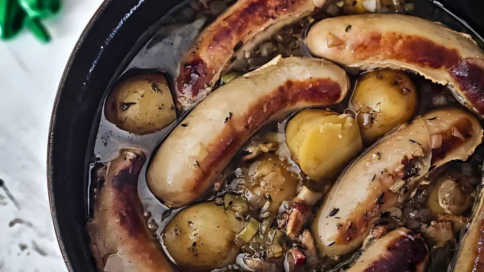 A dish with browned sausages and potatoes in a broth, garnished with herbs.