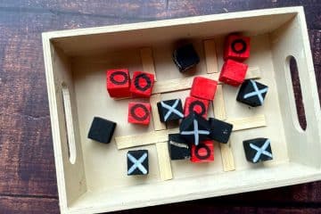 Wooden tray with small black and red blocks marked with X's and O's, arranged on a grid resembling a DIY tic-tac-toe board.