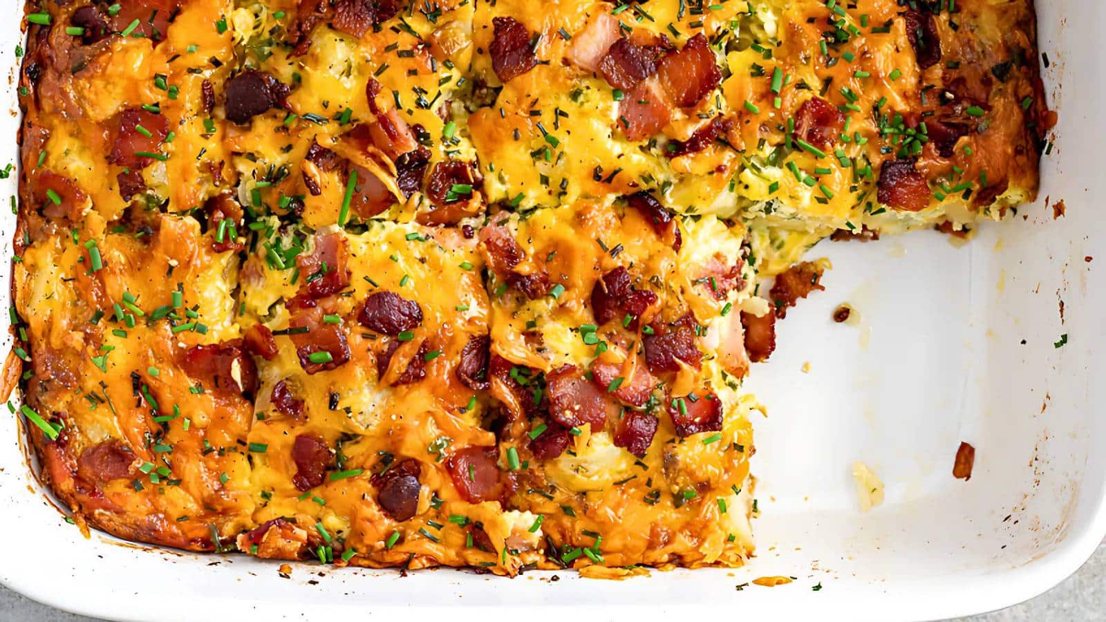 A baked casserole with a missing square piece. It features melted cheese, bacon bits, and garnished with chopped chives.