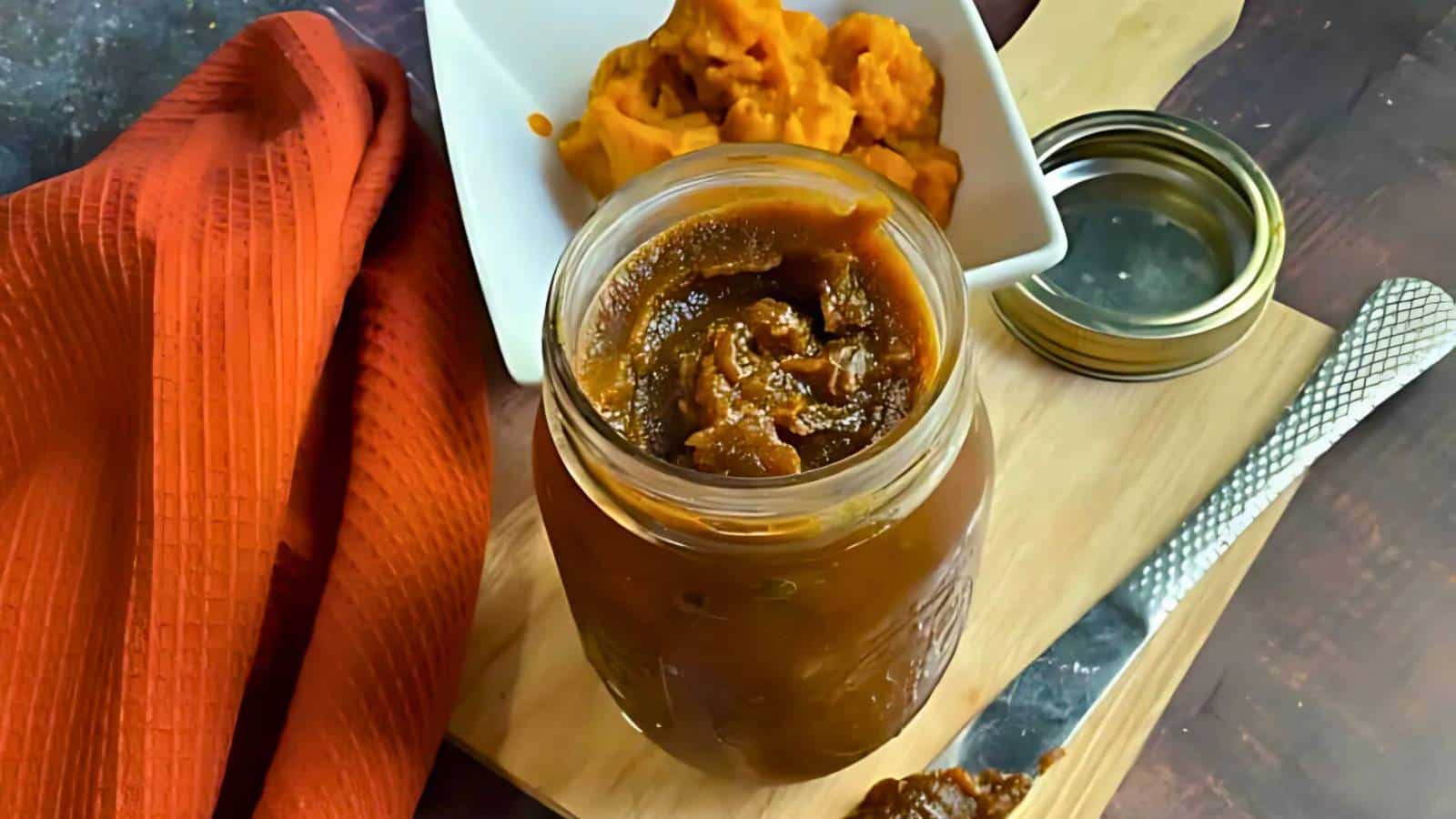 A jar of pumpkin butter on a wooden board with a small dish of pumpkin puree and an orange cloth beside it.