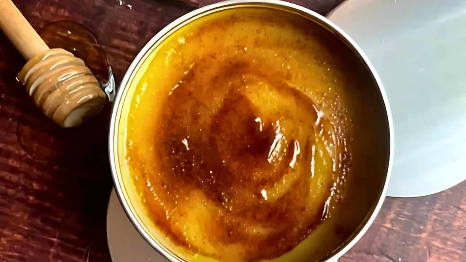 A tin filled with golden honey beside a honey dipper on a wooden surface.