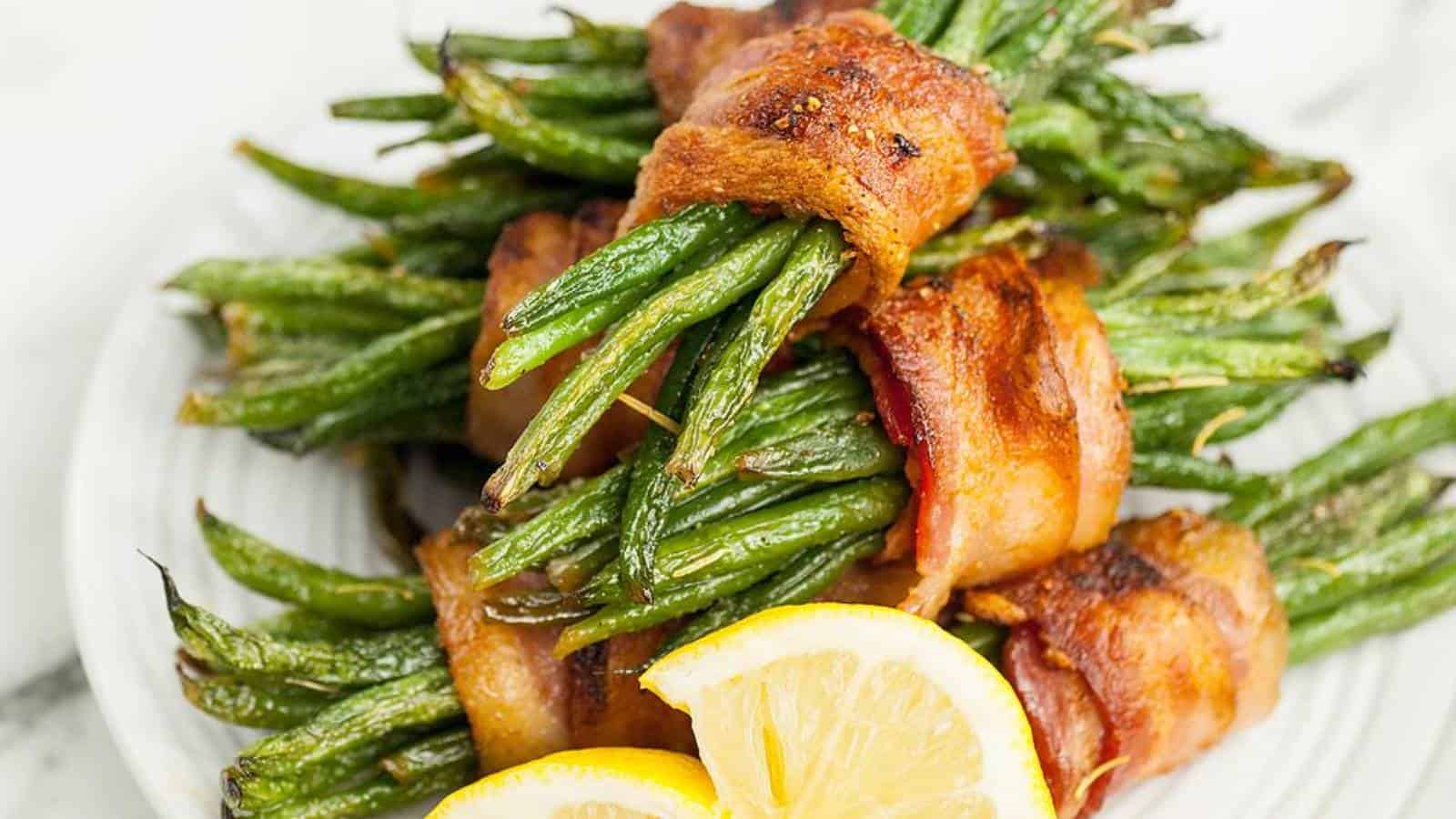 Bacon-wrapped green bean bundles served on a white plate with lemon slices.