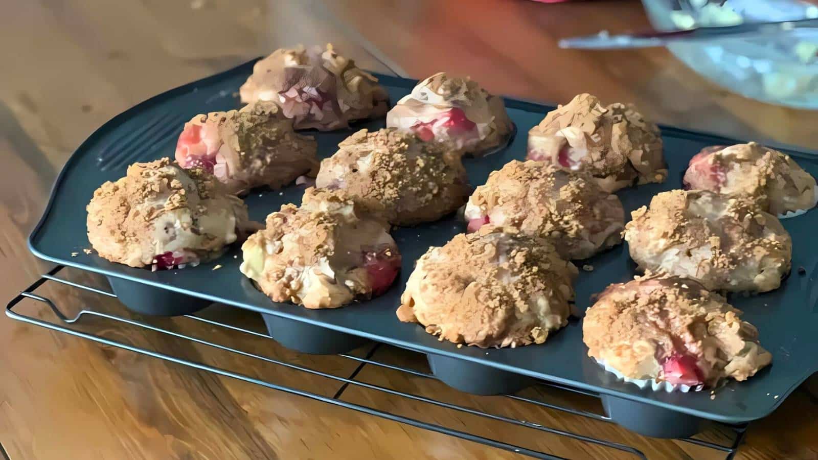 A tray of freshly baked muffins with crumbly toppings, cooling on a wire rack.