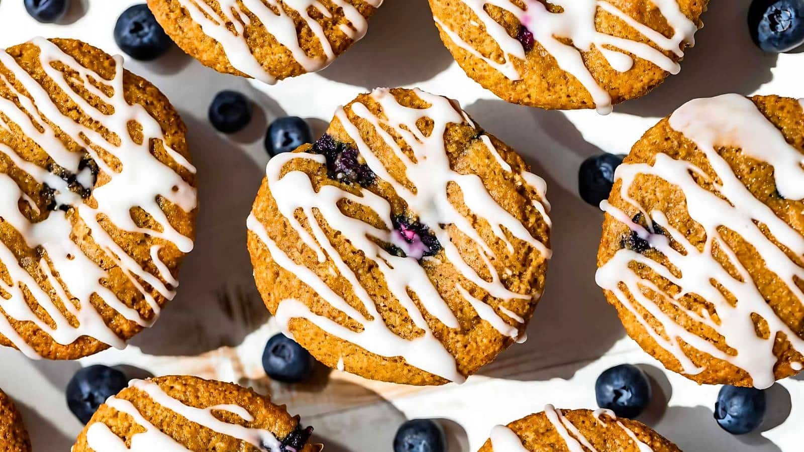 Top-down view of several iced blueberry muffins scattered with whole blueberries on a white background.
