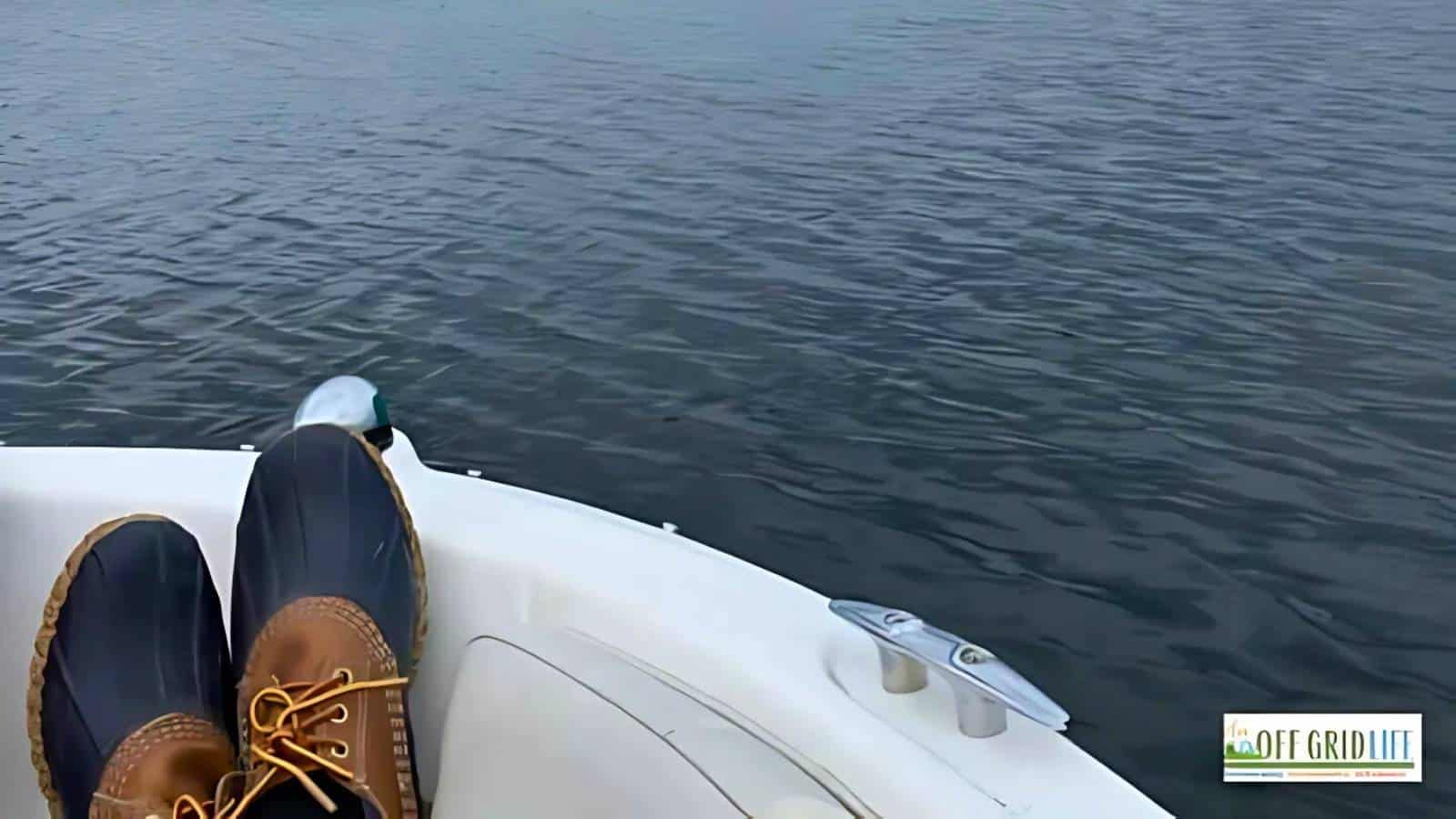 Person's feet in boots rest on a boat edge, overlooking calm water.