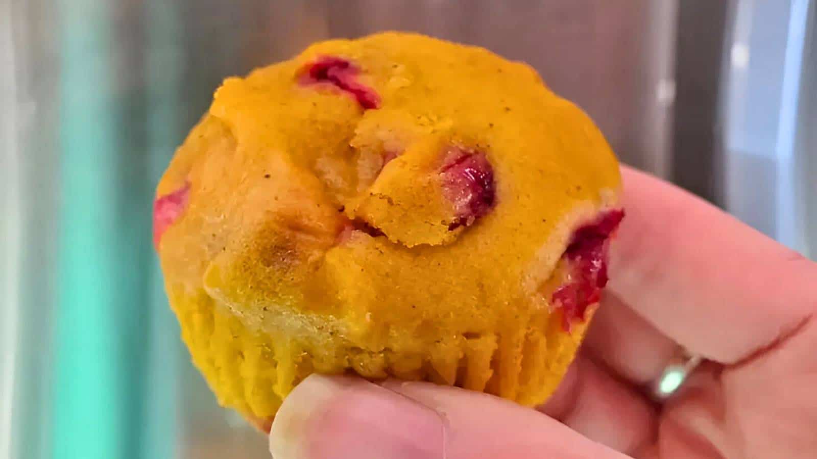 Close-up of a hand holding a yellow muffin with visible pieces of red fruit.