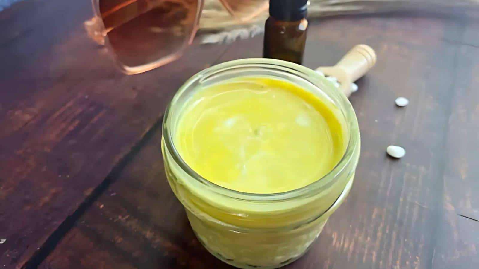 A mason jar filled with homemade mayonnaise sits on a wooden table next to a blue cloth.