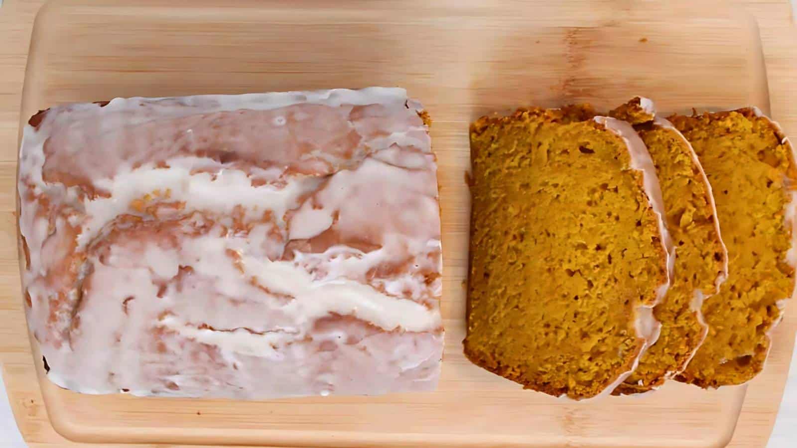 A glazed loaf of pumpkin bread, partially sliced, on a wooden cutting board.