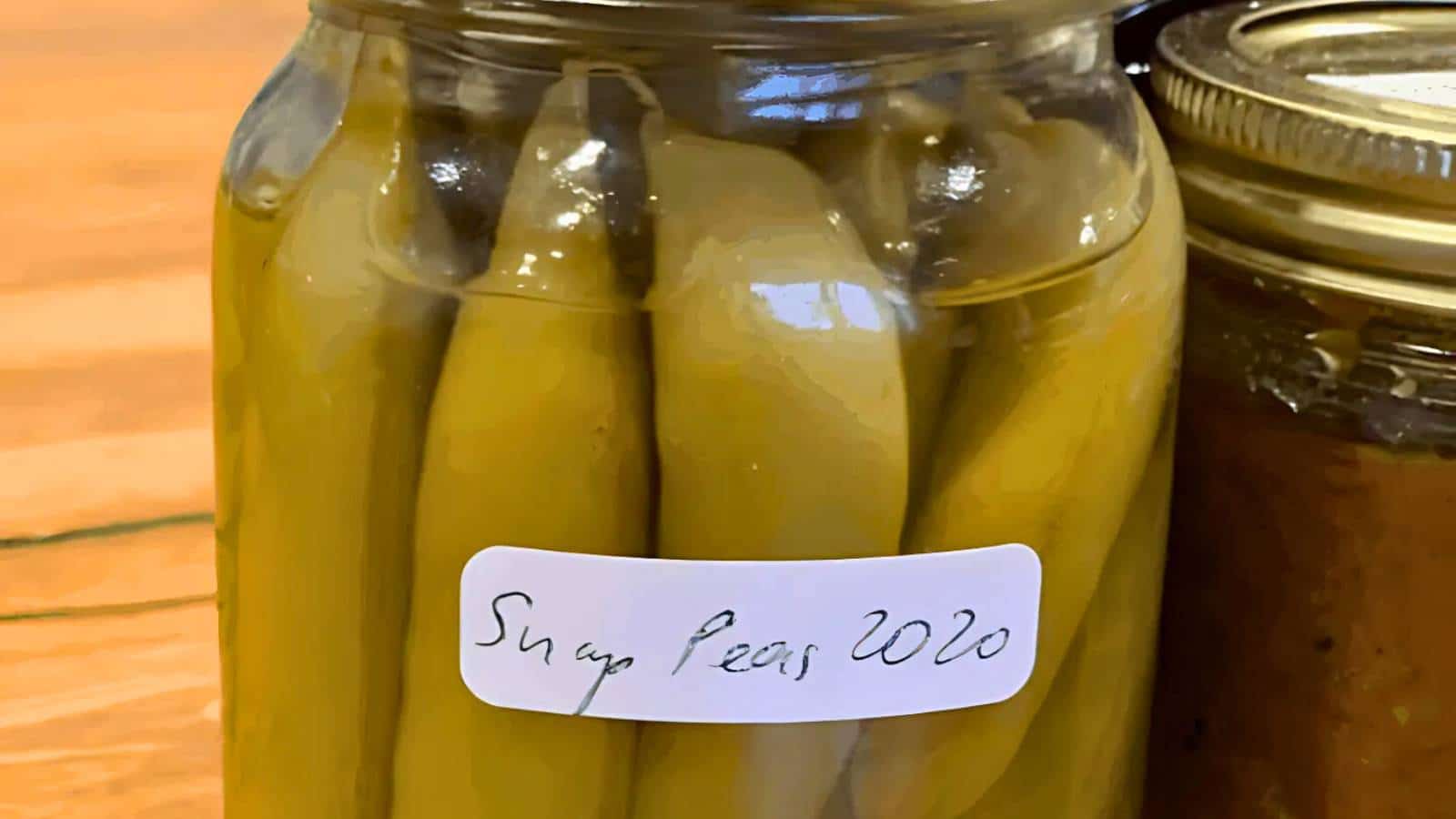A jar labeled "Snap Peas 2020" filled with pickled snap peas next to another jar.