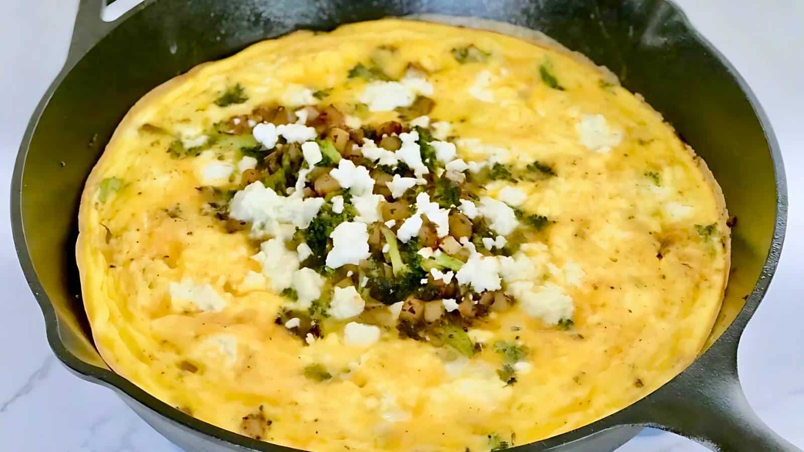 A frittata with vegetables and crumbled cheese on top in a black skillet.