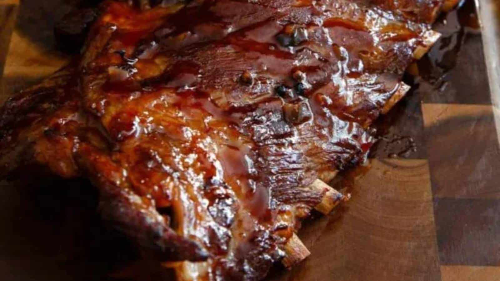 A rack of glazed, cooked ribs resting on a wooden cutting board.