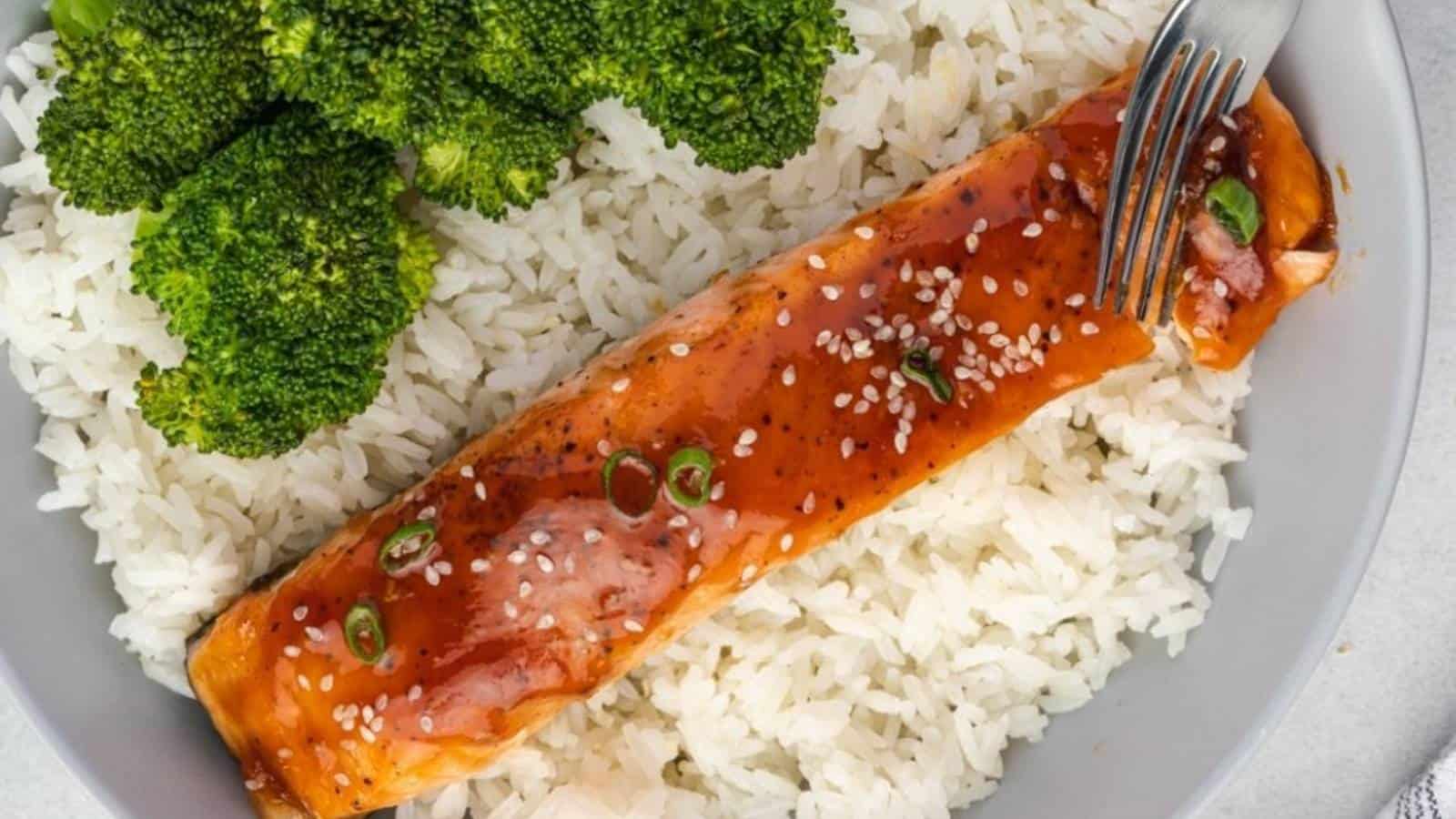 Salmon fillet glazed with sauce, topped with sesame seeds and green onions, served on white rice with broccoli.