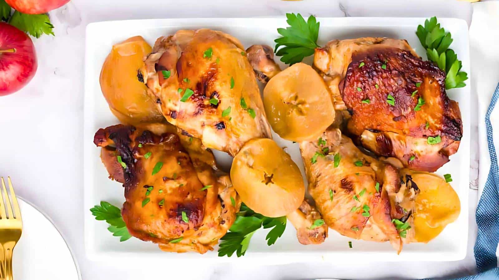 A platter of roasted chicken, garnished with parsley and accompanied by halved apples, on a white rectangular dish.