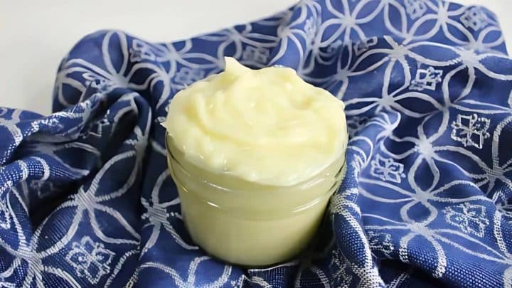 A small glass jar filled with creamy mayonnaise sits on a blue and white patterned cloth.