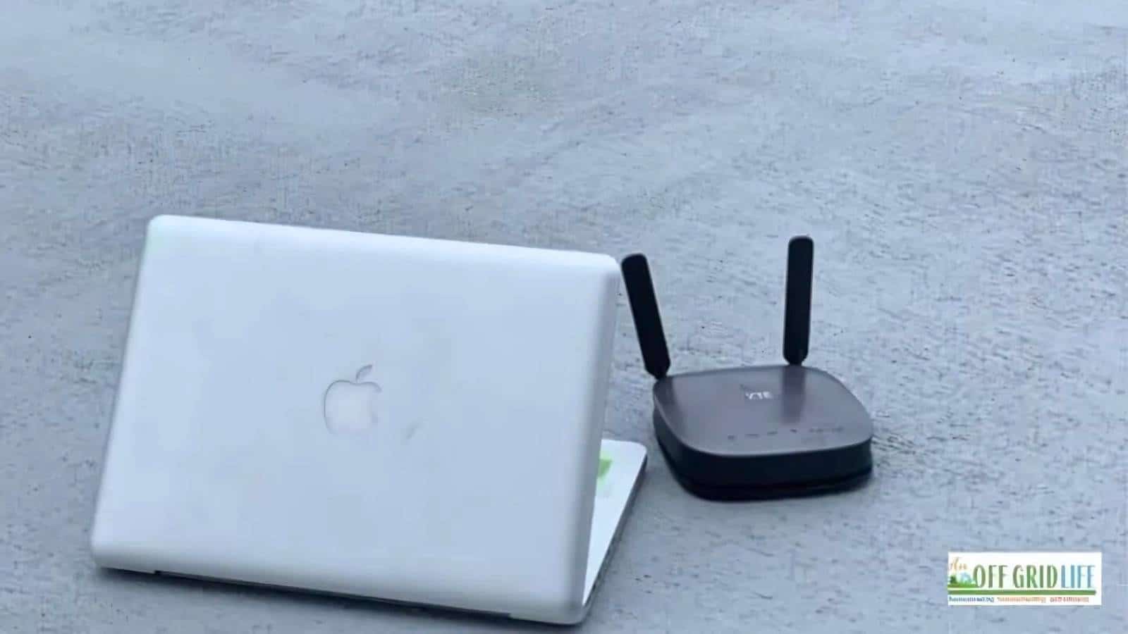 A closed white laptop with an Apple logo next to a small black router on a gray surface.