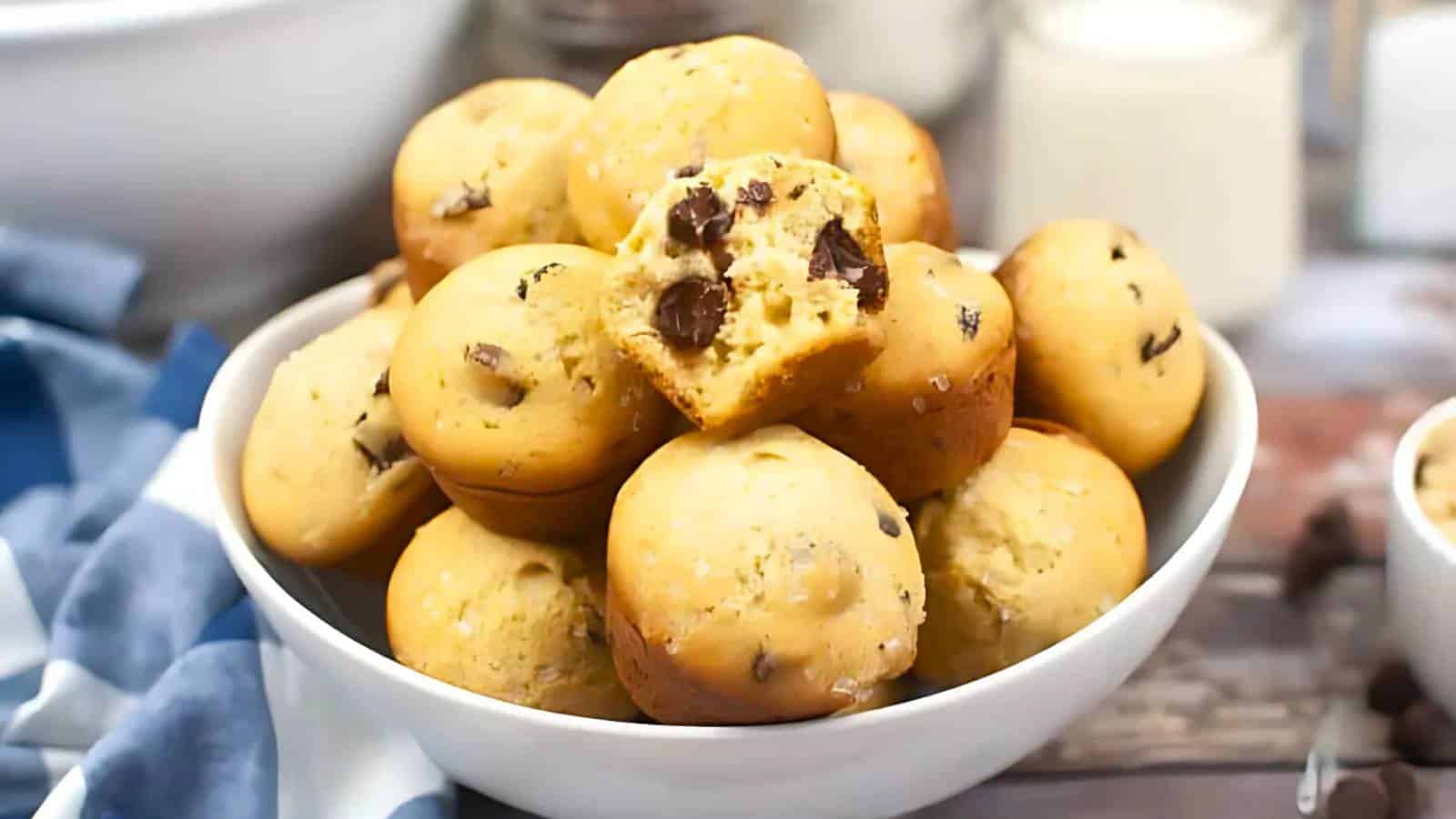 Chocolate chip cookies with visible chunks of chocolate and a sprinkle of sea salt, arranged on a baking sheet. One cookie is broken in half, showing its interior.