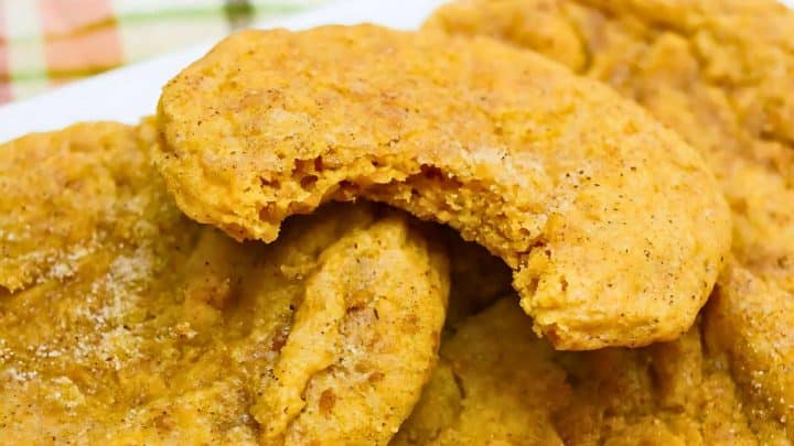 Close-up of several pumpkin cookies stacked, with one cookie on top having a bite taken out of it.