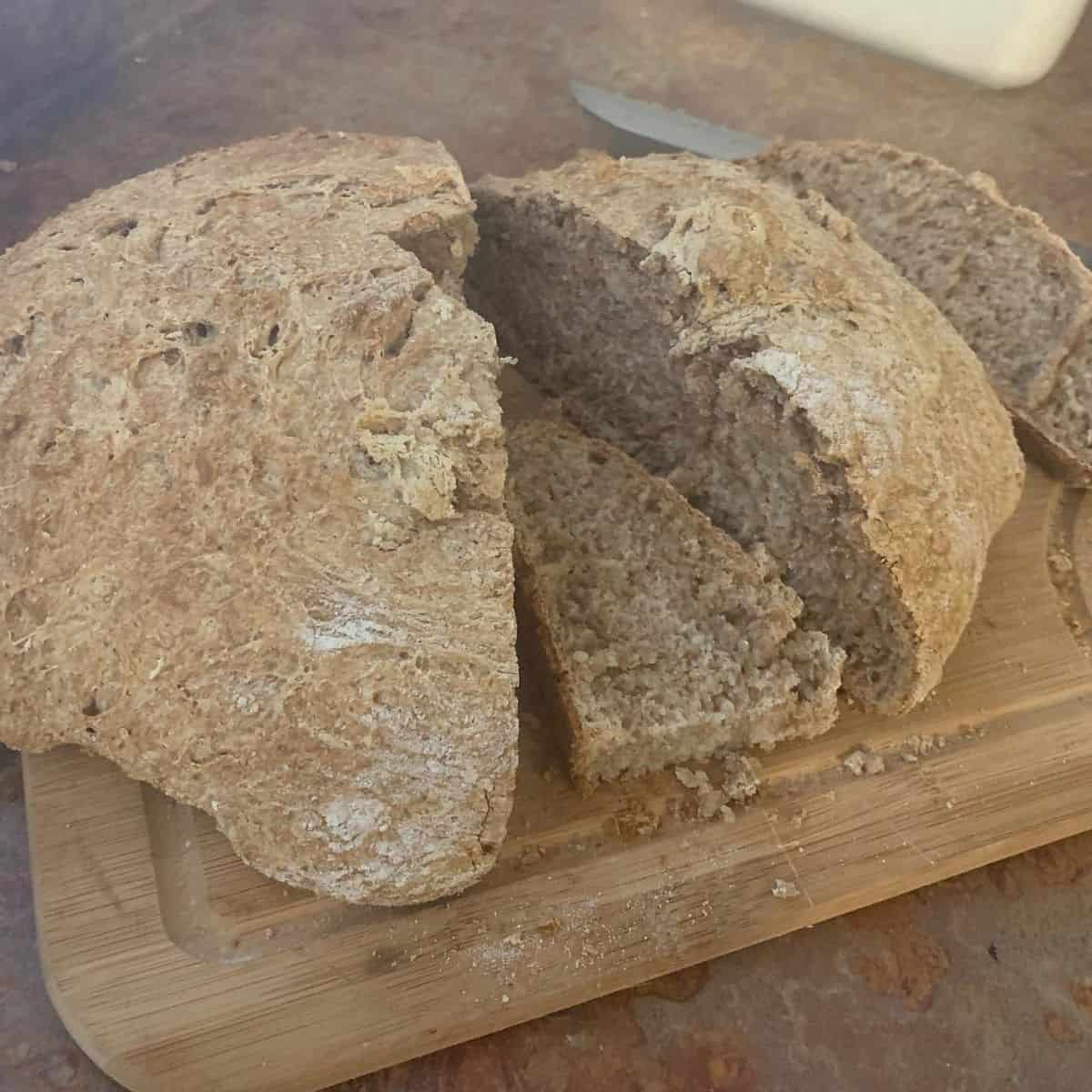 Sourdough bread, round loaf on wooden cutting board, cut with one slice