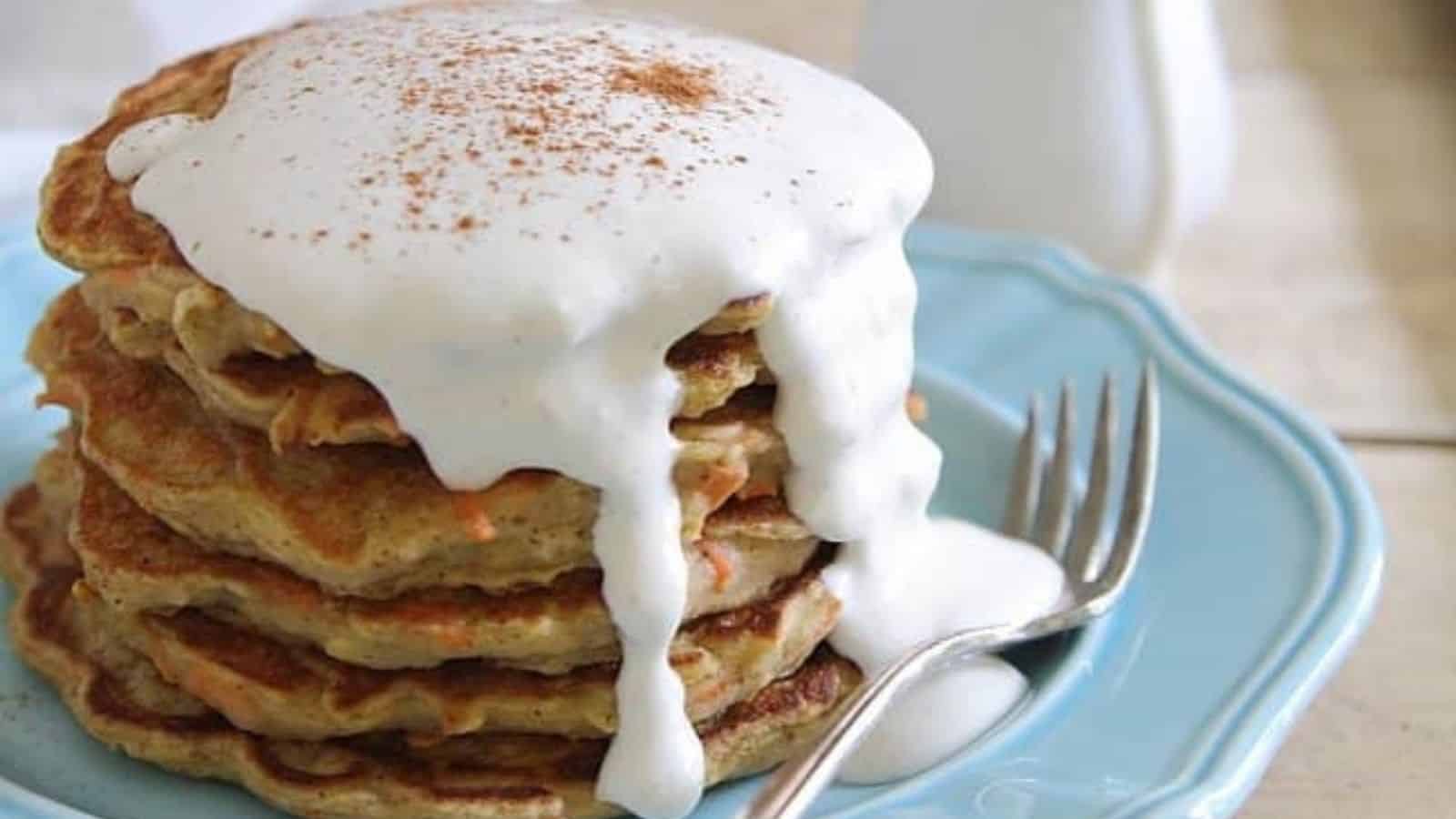 A stack of pancakes topped with a generous amount of white whipped cream and a sprinkle of cinnamon sits on a blue plate with a fork beside it.