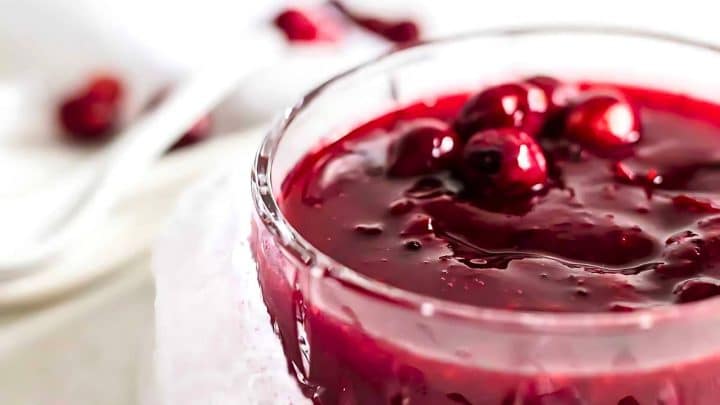 Close-up of a glass bowl filled with red berry jam, topped with whole berries.