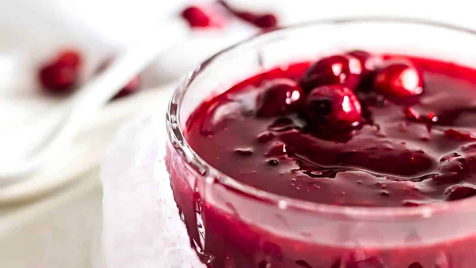 Close-up of a glass bowl filled with red berry jam, topped with whole berries.