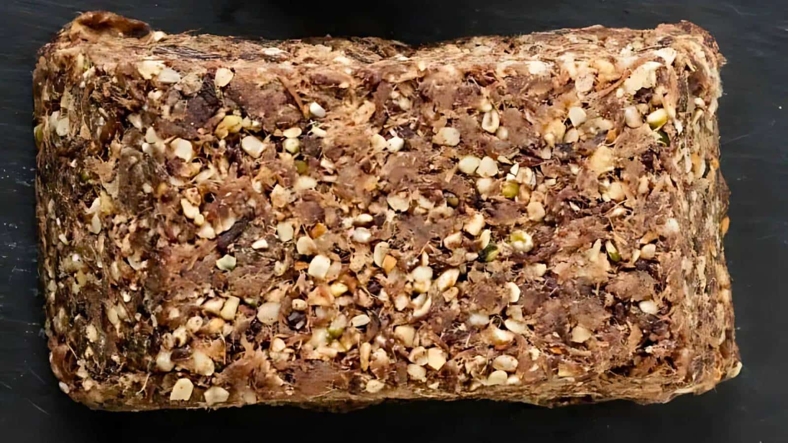 A rectangular loaf of dense, dark multigrain bread with visible seeds and grains on a black background.