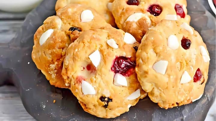 Cookies with white chocolate chunks and cranberries on a dark plate.