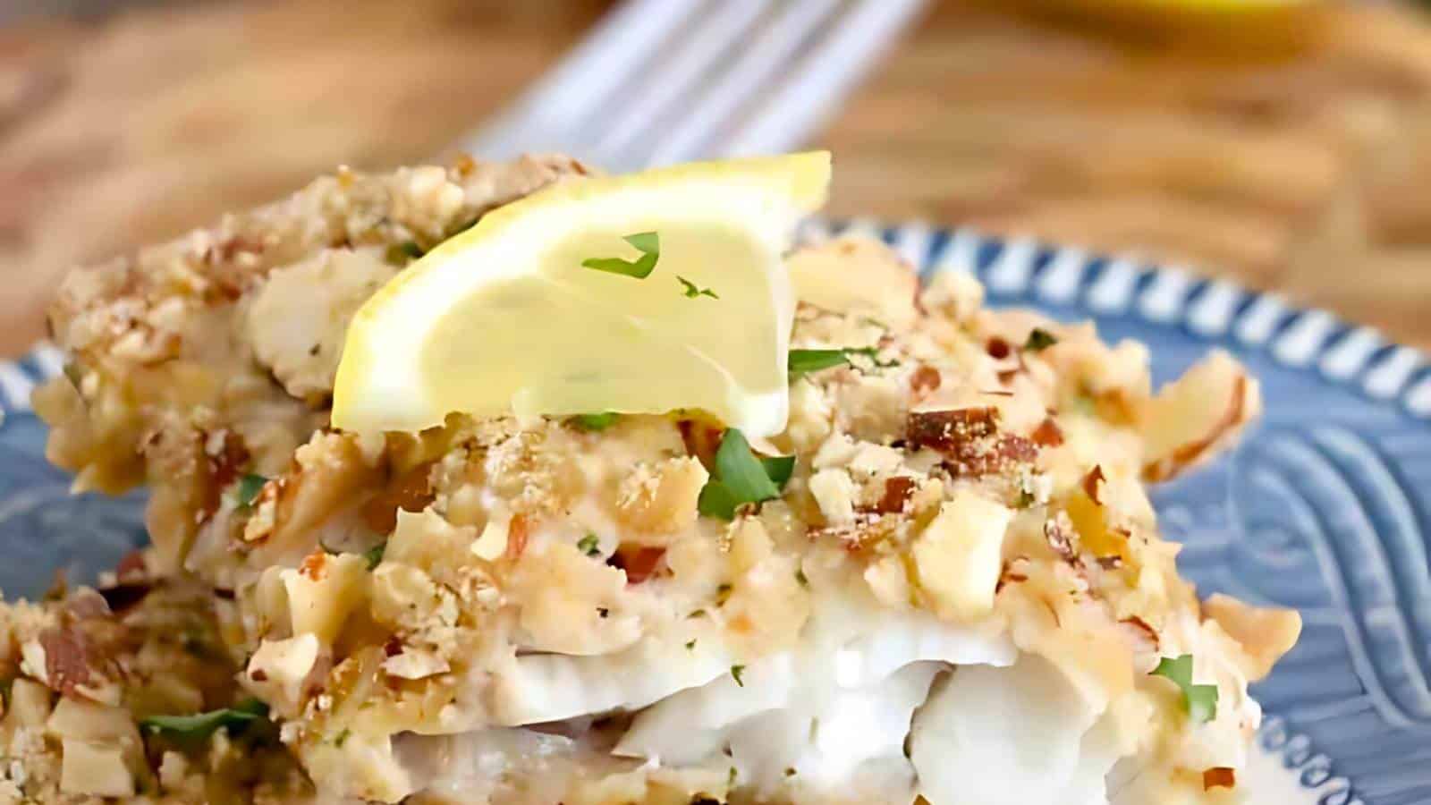Close-up of a plate with a piece of almond-crusted fish garnished with a lemon wedge and herbs.