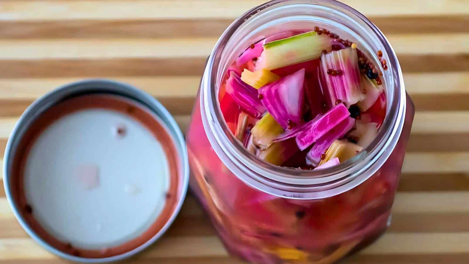 Open jar of pickled vegetables with various colors on a striped wooden surface, lid placed beside it.