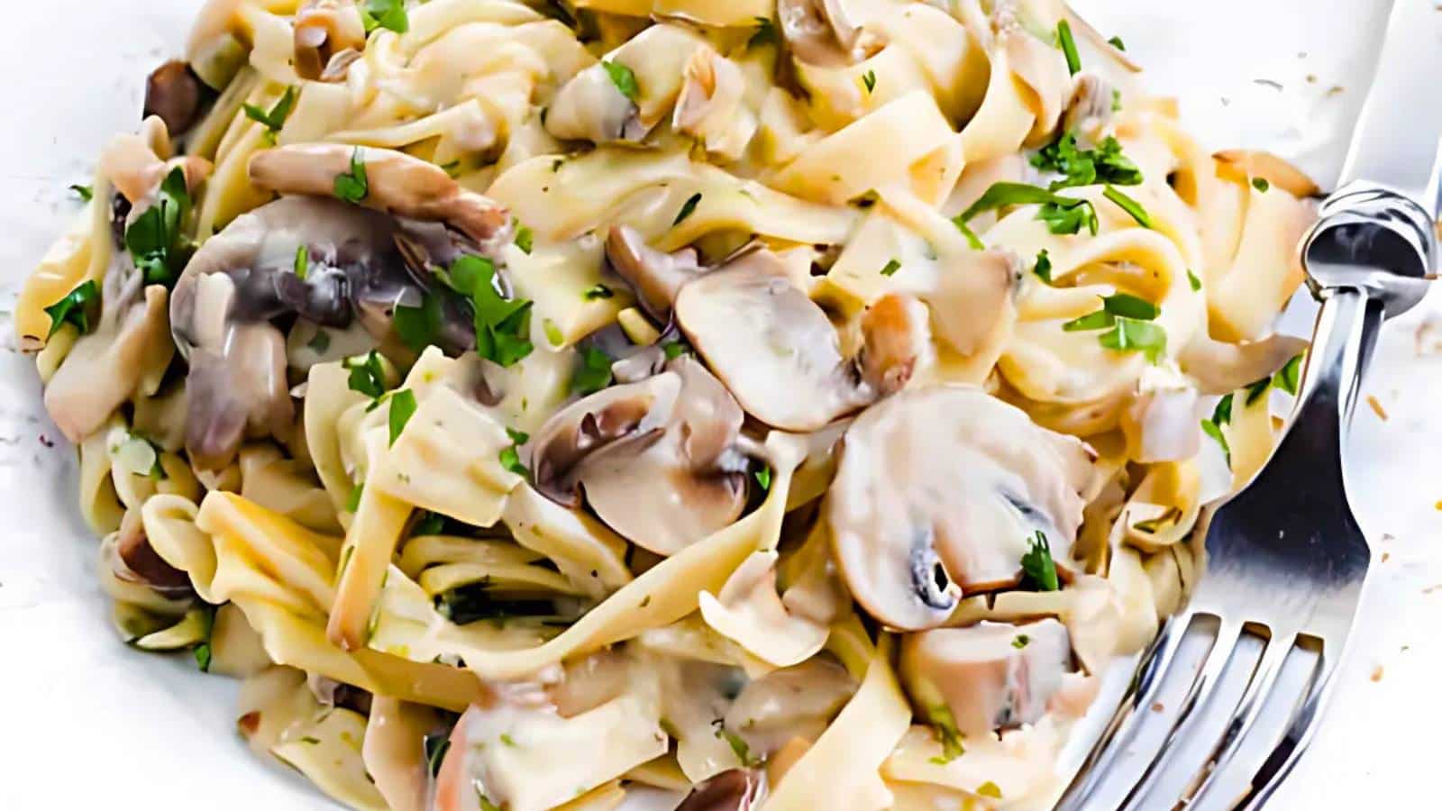 A plate of fettuccine with creamy mushroom sauce, garnished with chopped parsley, and a fork on the side.
