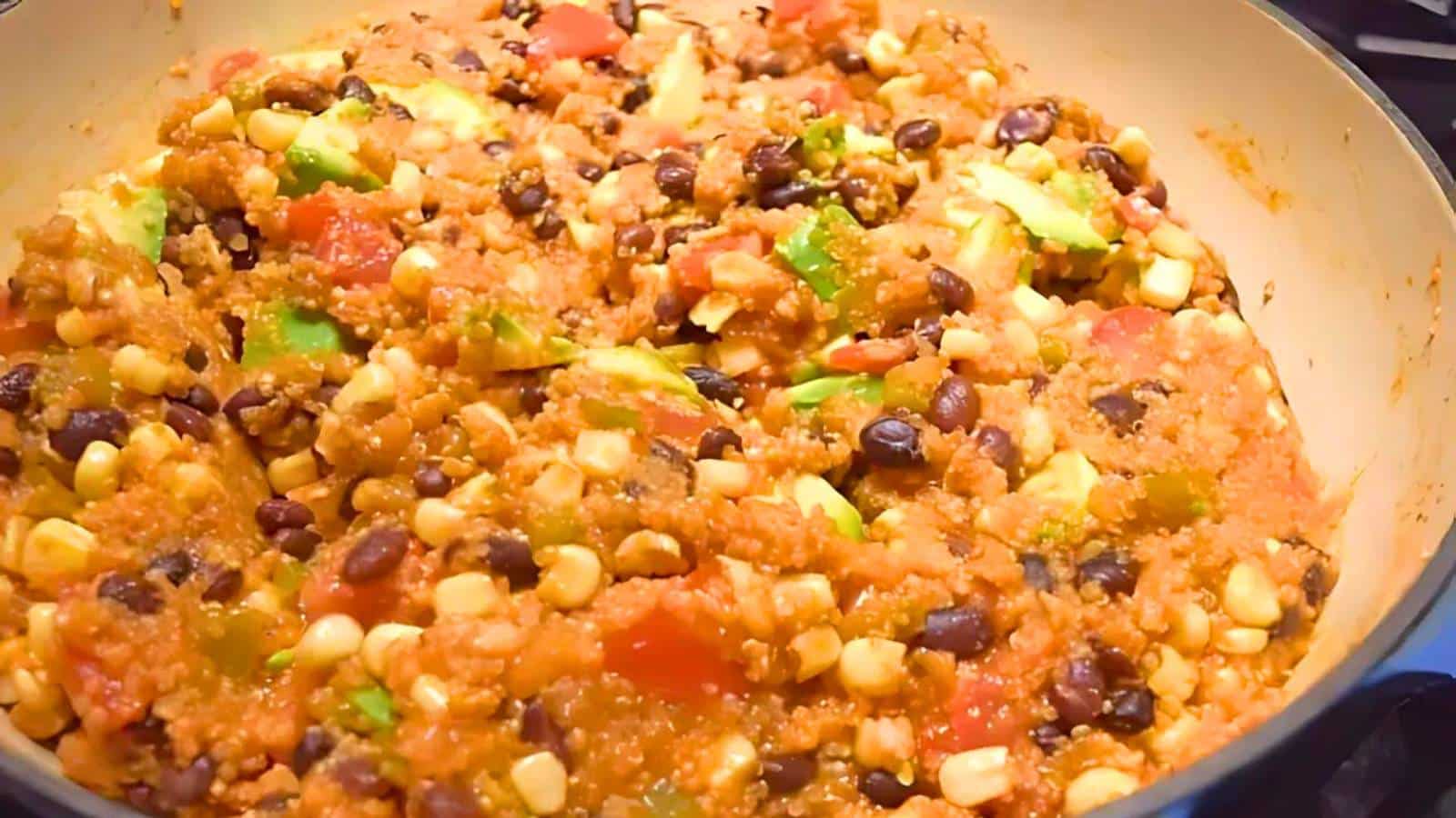 A pot filled with a mixture of quinoa, black beans, corn, diced tomatoes, and green bell peppers, all cooked together.