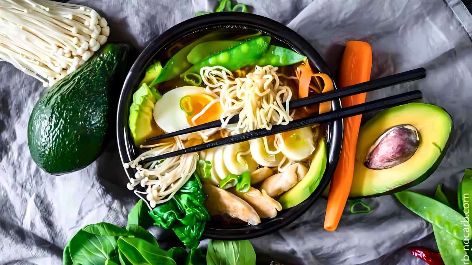Bowl of ramen with noodles, boiled egg, vegetables, and chopsticks. Surrounded by avocado, carrots, greens, and enoki mushrooms.