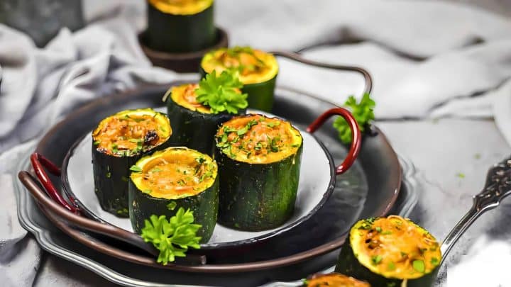 Several stuffed zucchini cups garnished with parsley are arranged on a white plate with a black handle.