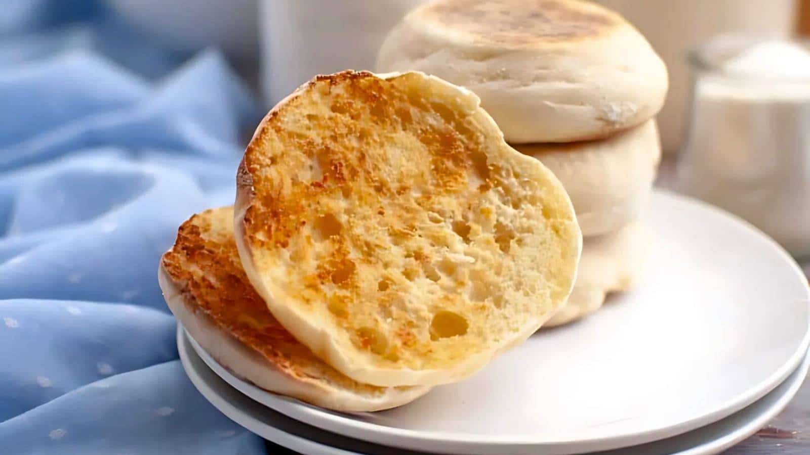 A close-up of toasted English muffins on a white plate, with a blue cloth in the background.