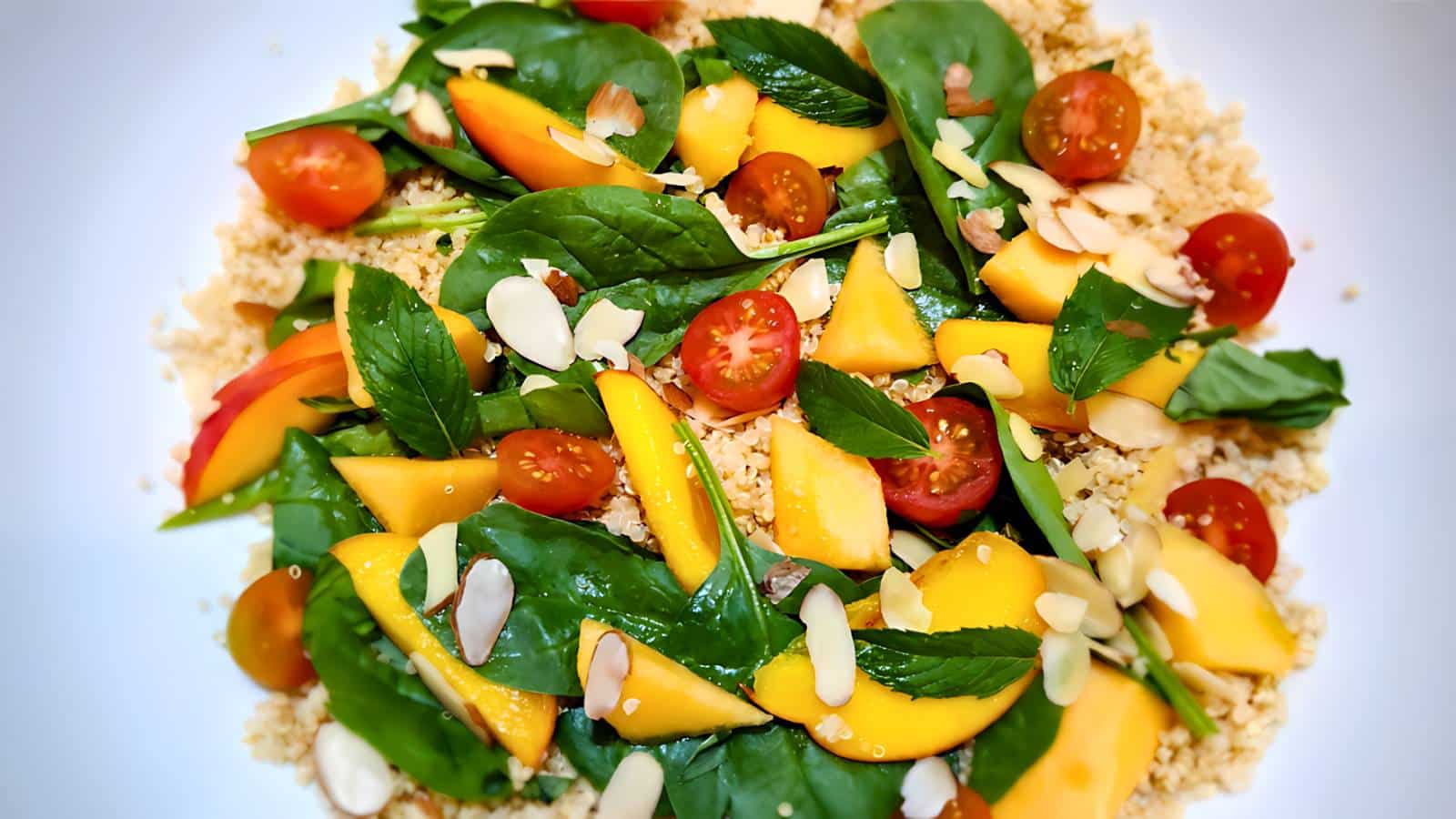 A vibrant plate of couscous topped with spinach, mango slices, cherry tomatoes, and almond slivers.