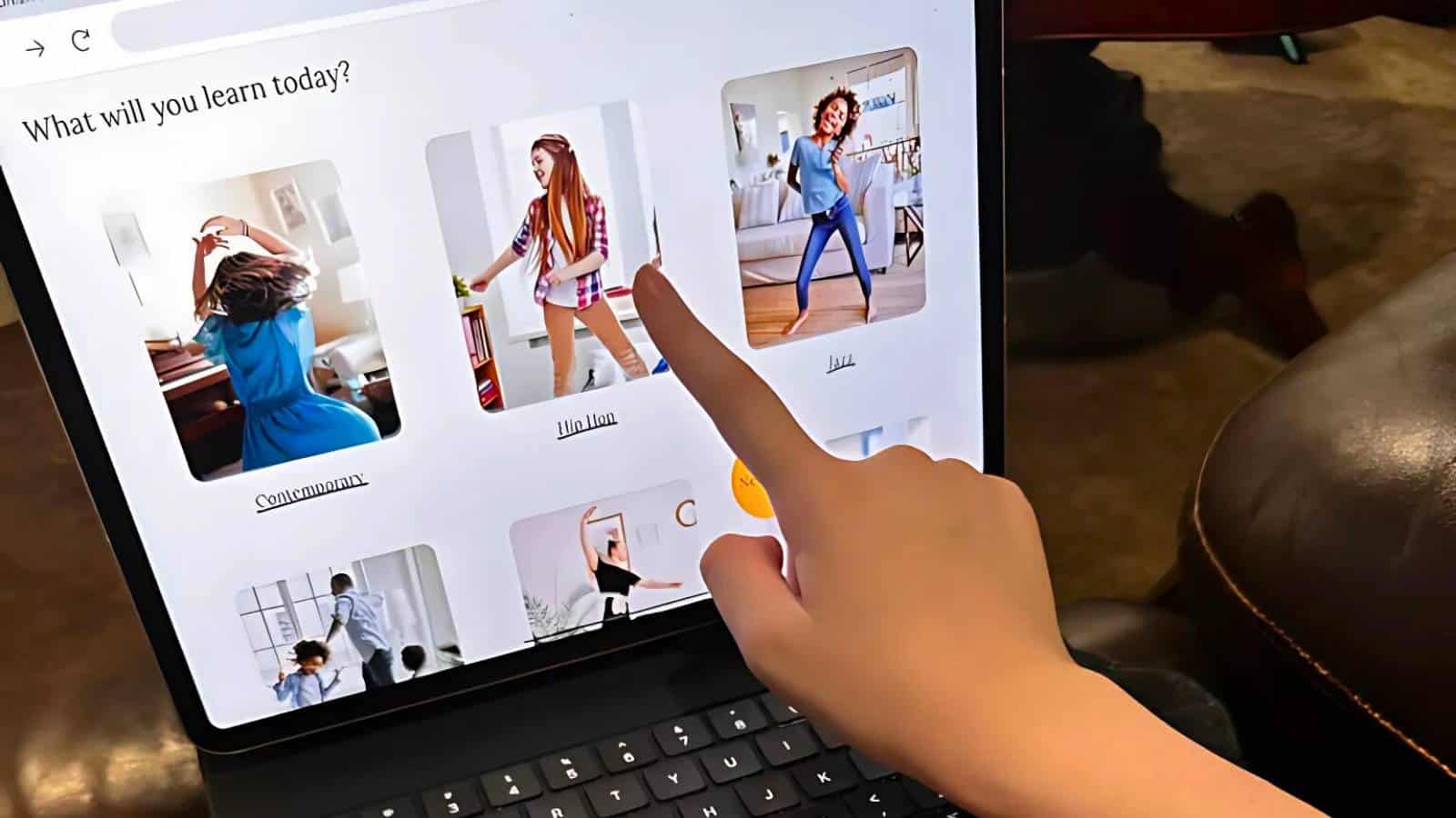 A person points at a laptop screen displaying a dance website offering classes titled Contemporary, Hip Hop, and Jazz.